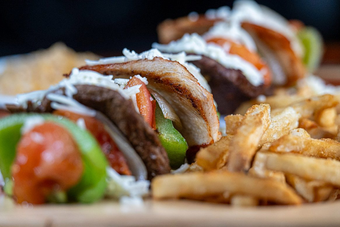 Juan's Authentic Mexican Restaurant Mississippi - Close-up of gyros filled with sliced meat, tomatoes, green peppers, and topped with white sauce, served alongside a pile of golden French fries at an authentic Mexican food spot in Biloxi, Mississippi.