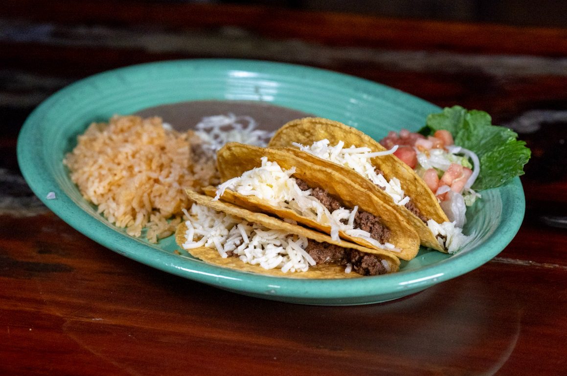 Juan's Authentic Mexican Restaurant Mississippi - A green plate with two hard shell tacos filled with ground beef and shredded cheese, served with Mexican rice, refried beans, and fresh pico de gallo—experience authentic Mexican food Biloxi Mississippi style.